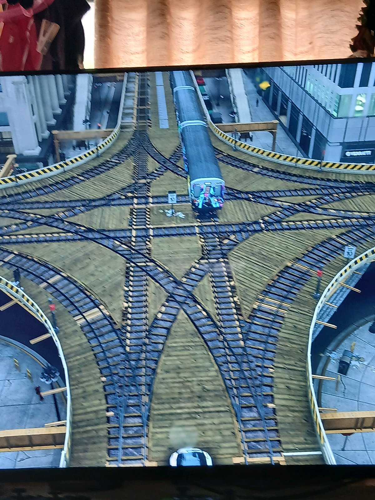 Need for Speedのレイクショア風の街中で、巨大な複数線路のジャンクション上に列車が停車しているゲーム画面。前面にトミカの話題を添えた投稿文脈で、シカゴをモデルにした都市のような景観が映っている。