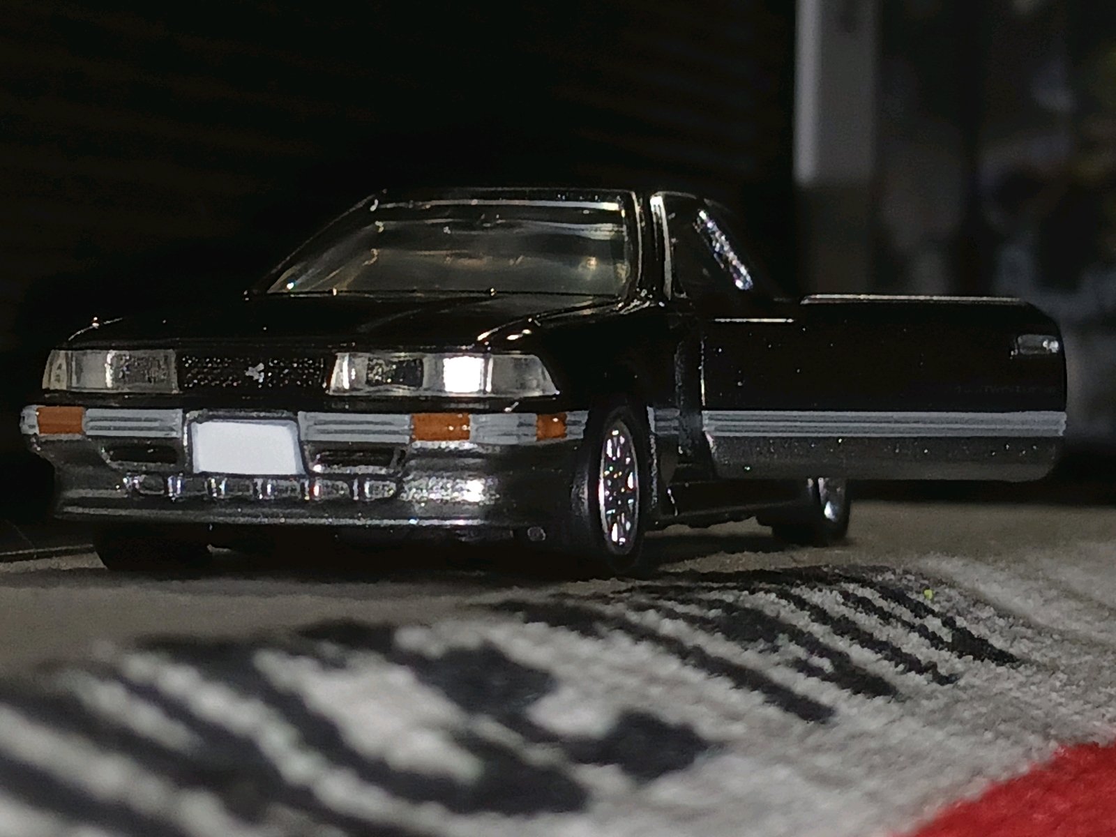 黒いトヨタ・ソアラ Z20 3.0GT TwinTurboのミニカーが、暗い背景の中で斜め前から写されている。フロントのシルバー加飾が目立ち、高級感のあるクーペとして紹介されている。